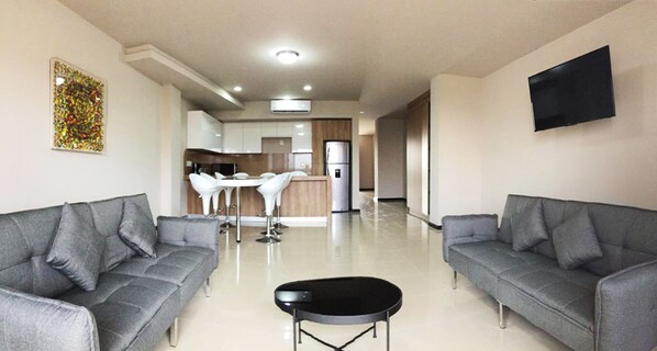 A modern living room with grey sofas, a black coffee table, and a kitchen area in the background.