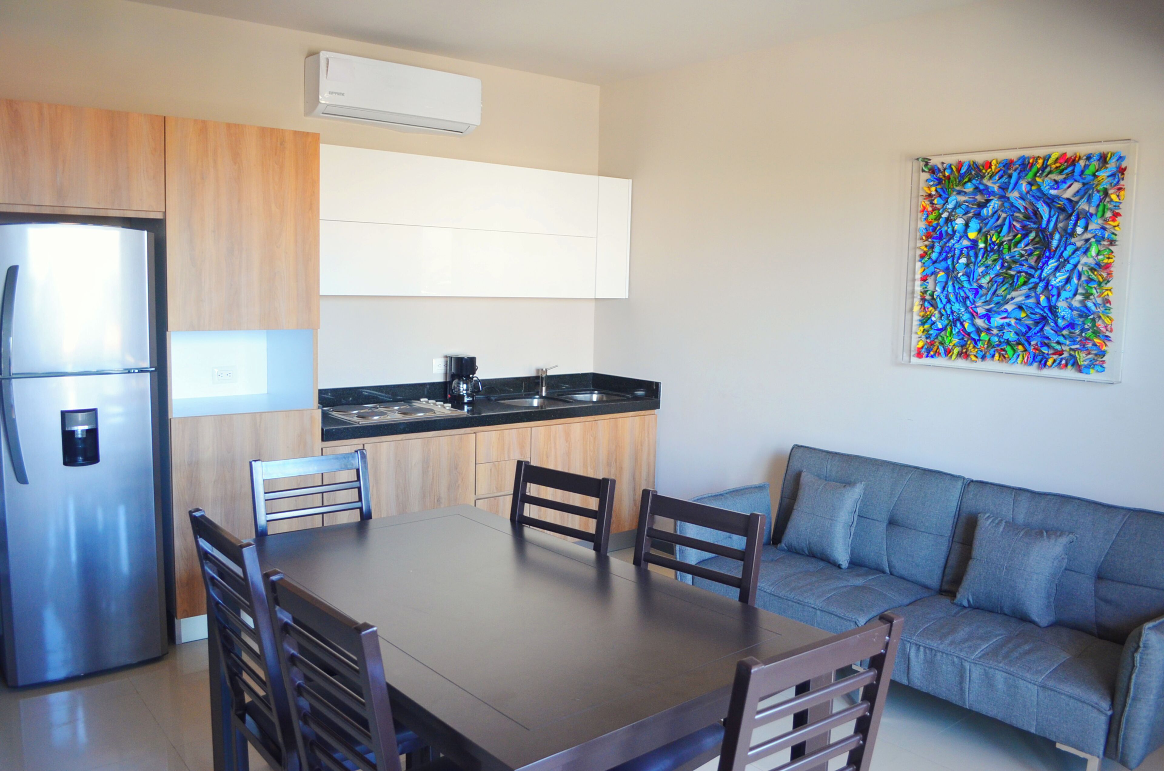 Una cocina moderna con refrigerador, estufa y pileta. Hay una mesa de comedor con sillas y un sofá.
