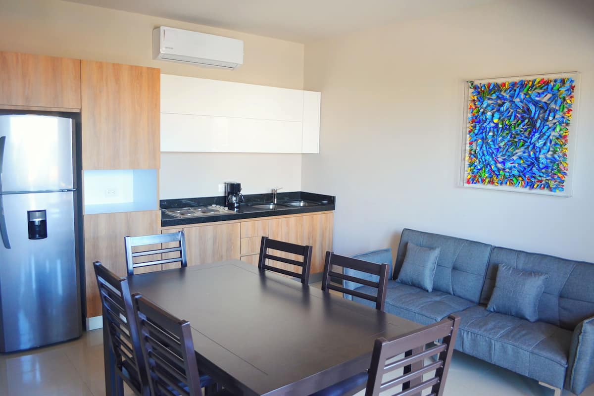 Una cocina moderna con refrigerador incorporado, una mesa de comedor con sillas y un sofá gris.
