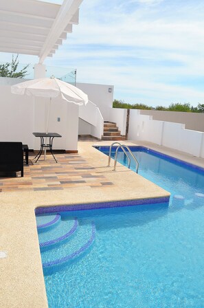 A swimming pool with a tiled edge, a white umbrella, and a table with chairs. - Bahia Marina Departamentos (Mazatlán)