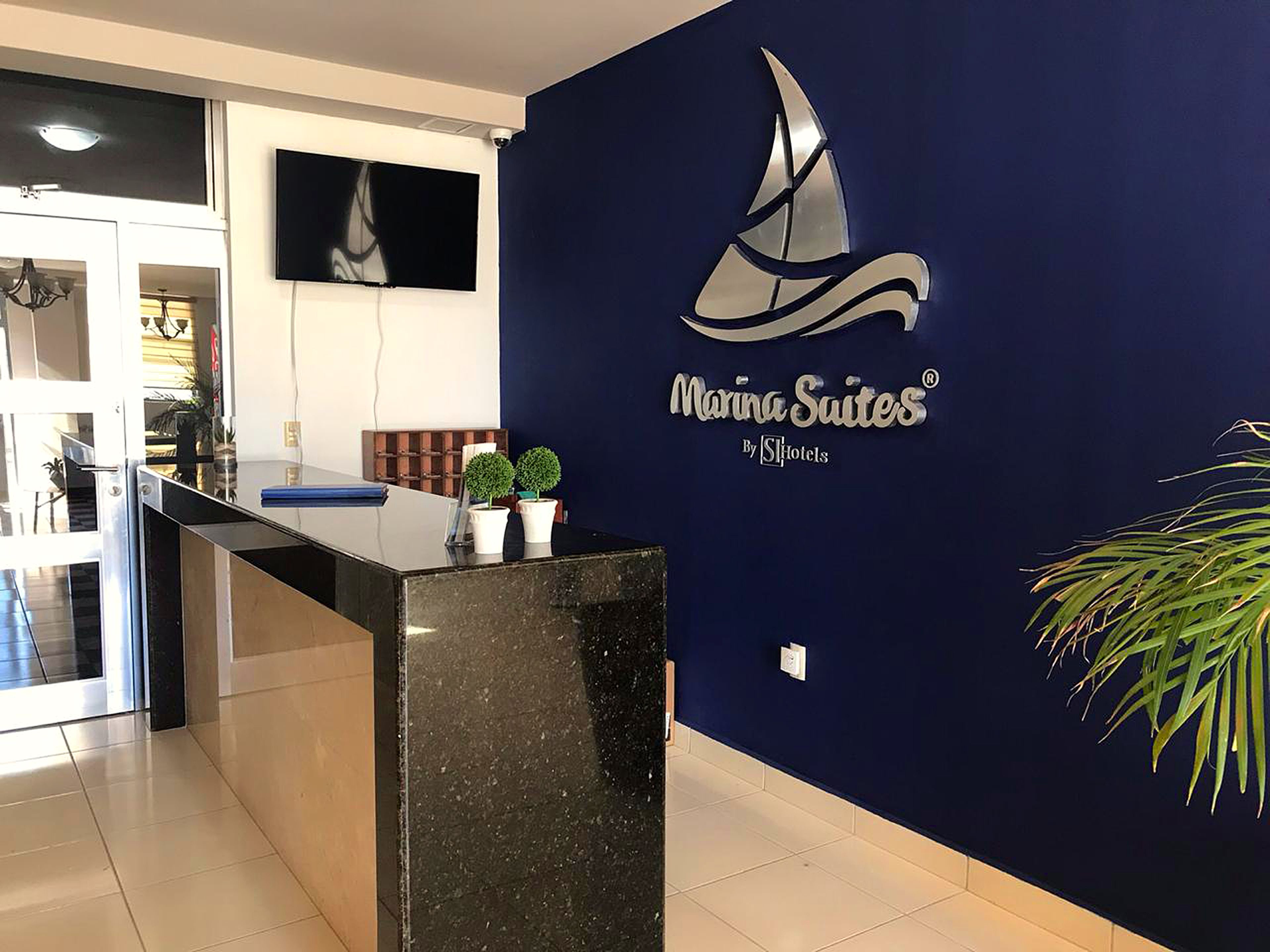 A reception desk with a dark blue wall featuring the Marina Suites logo and a sailboat graphic.