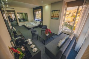 A modern hotel room with a bed, seating area, dining table, and a city view.