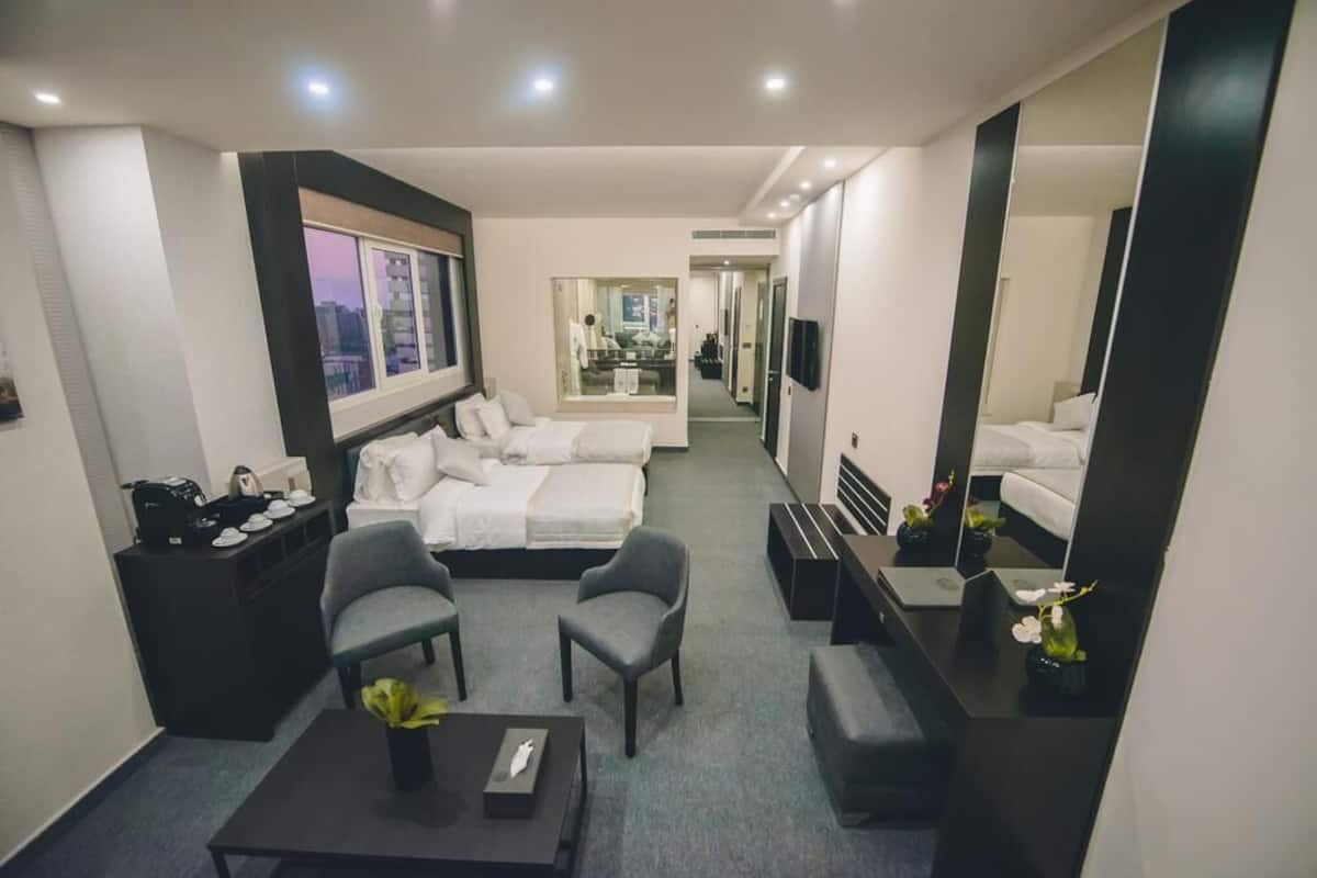 Una habitación de hotel moderna con una cama, dos sillones, una mesita de centro y un televisor.