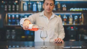 Un bartender sirve una bebida en un vaso detrás de una barra con estantes llenos de botellas.
