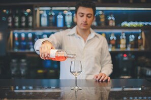Un bartender sirve una bebida en un vaso detrás de una barra con estantes llenos de botellas.