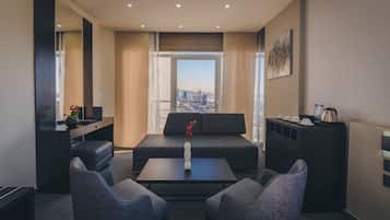A modern hotel room with a sofa, two armchairs, a coffee table, a TV, and a desk with a mirror.