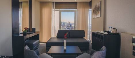 Una habitación de hotel moderna con un sofá, dos sillones, una mesa de centro, un televisor y un escritorio con un espejo.