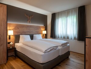 A double bed with a wooden headboard, two bedside lamps, a wall-mounted deer head decoration, and a window with curtains. - Pradas Resort Brigels, (Breil/Brigels), 65055B by Interhome (Breil/Brigels)