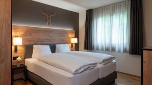 A hotel room with a large bed, two bedside lamps, a wooden headboard, a mounted deer head, and a window with curtains. - Pradas Resort Brigels, (Breil/Brigels), 65055B by Interhome (Breil/Brigels)