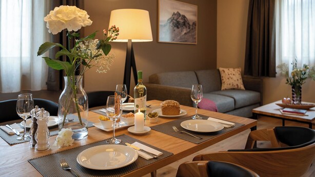 A dining area with a table set for two, a vase with flowers, a candle, and a lamp. - Pradas Resort Brigels, (Breil/Brigels), 65055B by Interhome (Breil/Brigels)