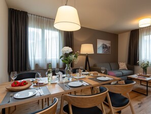 A dining area with a table set for two, a vase with flowers, and a painting on the wall.