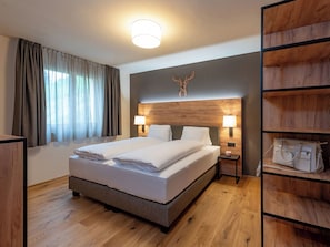 A hotel room with a large bed, two bedside lamps, a wooden headboard, a wooden floor, and a built-in wardrobe with shelves.