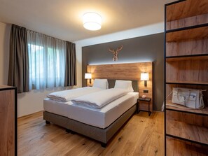 A hotel room with a bed, two bedside lamps, a wooden headboard, a large mirror, a wardrobe, and a window with curtains. - Pradas Resort Brigels, (Breil/Brigels), 65055B by Interhome (Breil/Brigels)
