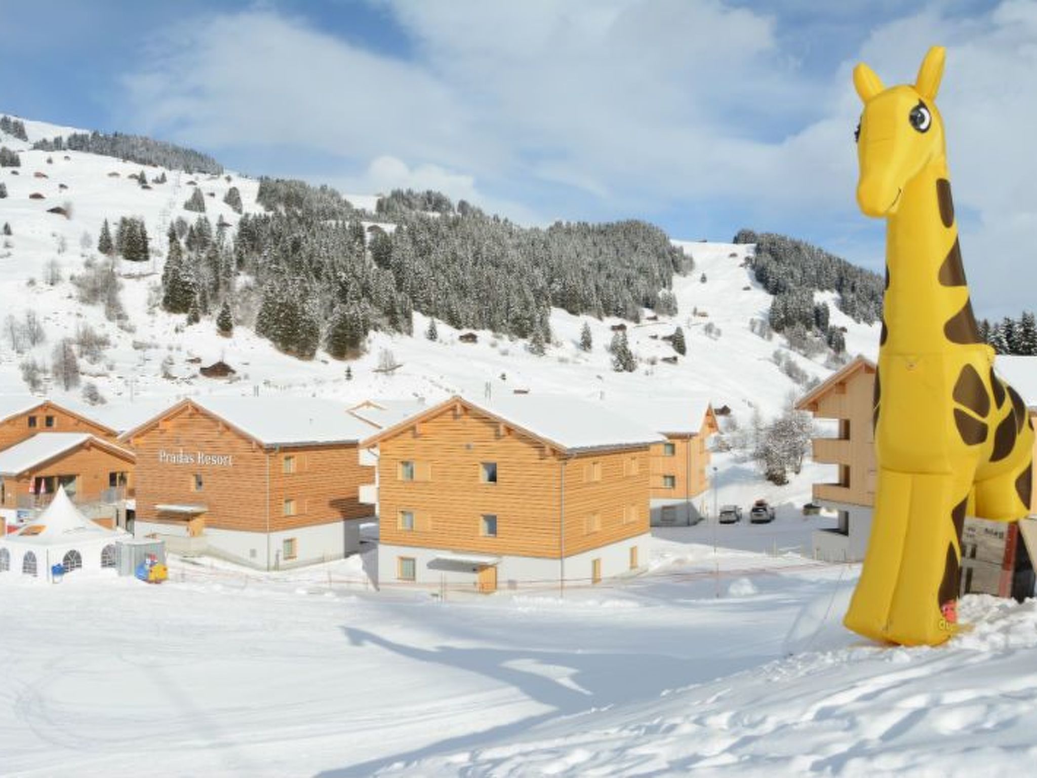 A wooden building with a sign reading 'Pradas Resort' in a snowy landscape with a giraffe statue.