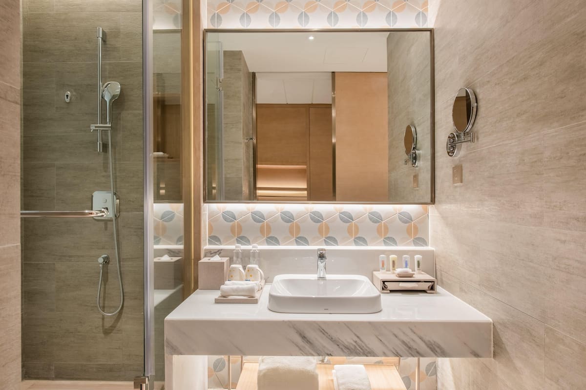 Un baño moderno con ducha de vidrio, lavamanos de mármol y un espejo grande.