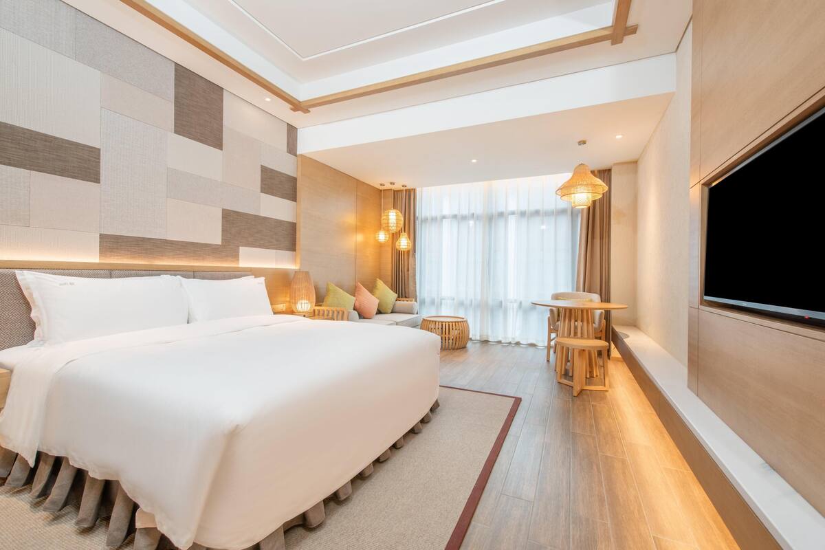 Una habitación de hotel moderna con una cama grande, un televisor, una mesita y un sofá.