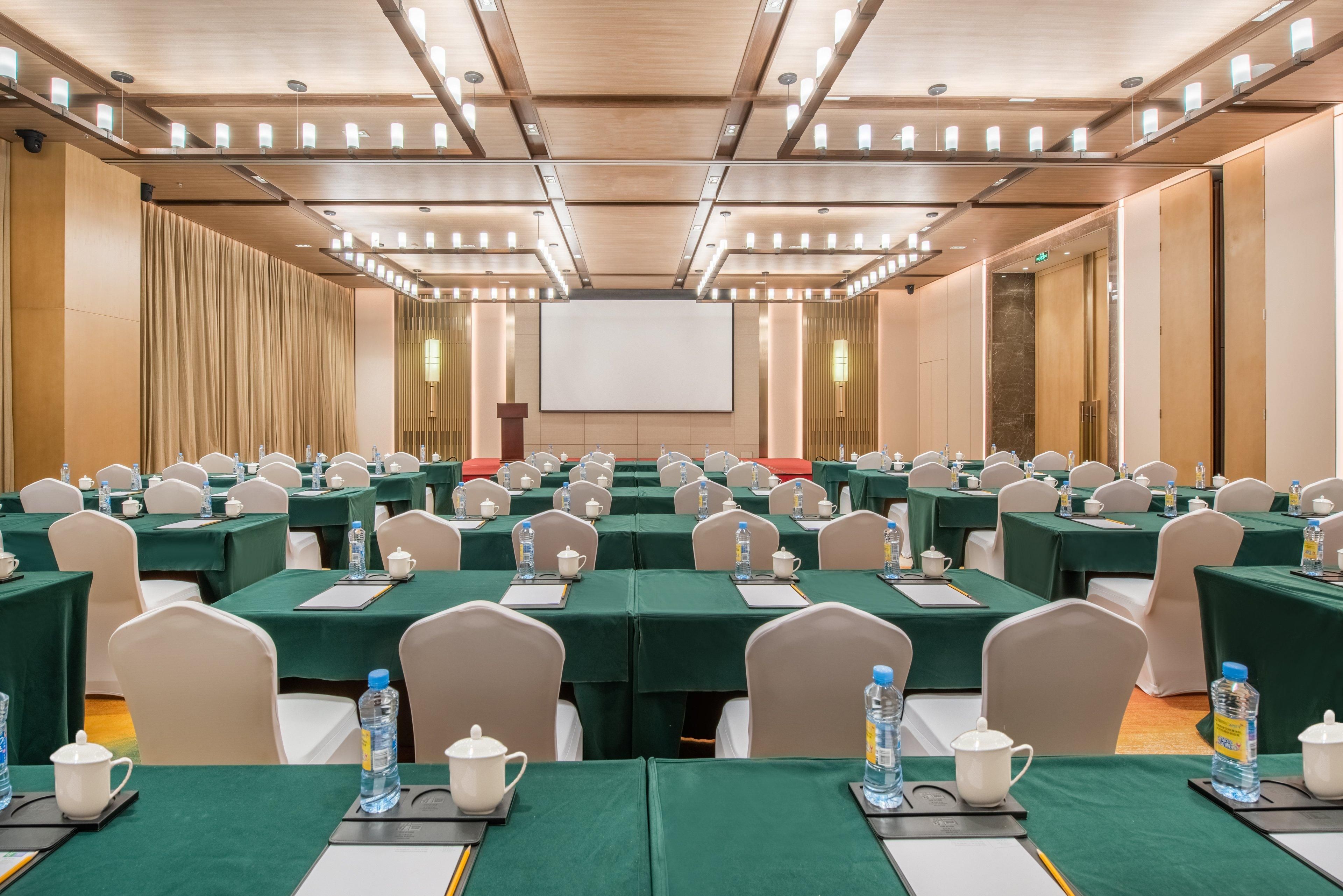 A conference room with rows of tables, chairs, and a large screen at the front.
