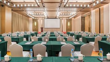 Un salón de conferencias con filas de mesas, sillas y una pantalla grande al frente.