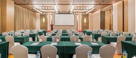 Une salle de conférence avec des rangées de tables, des chaises et un grand écran à l’avant.