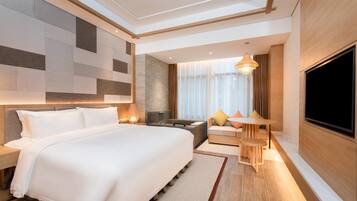 A modern hotel room with a large bed, a seating area with a table, a TV, and a large window with curtains.