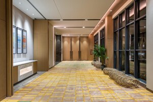 Corredor de hotel com piso estampado, painéis de madeira e grandes janelas.