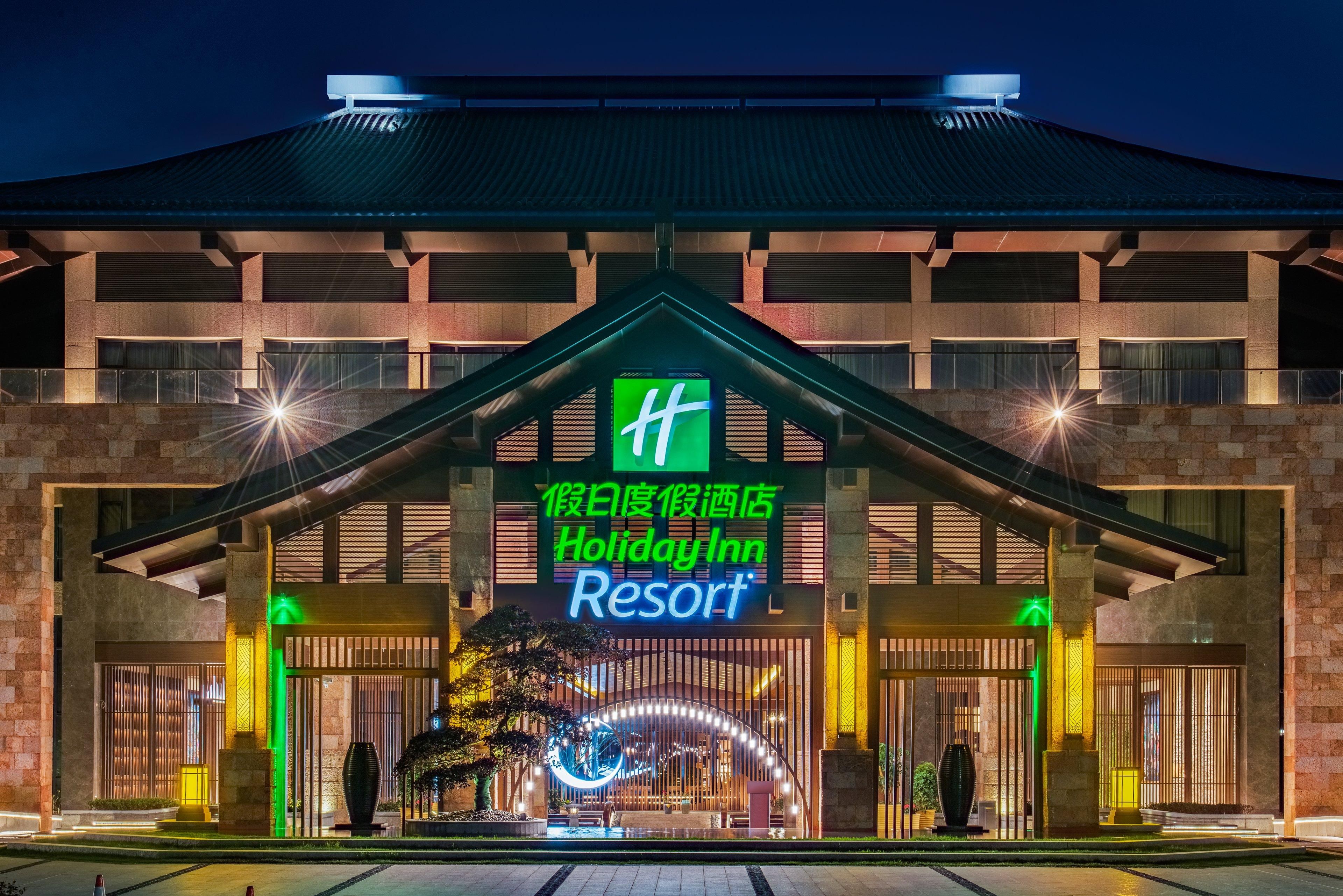 Um resort Holiday Inn com uma placa grande, entrada com portão e fachada bem iluminada.