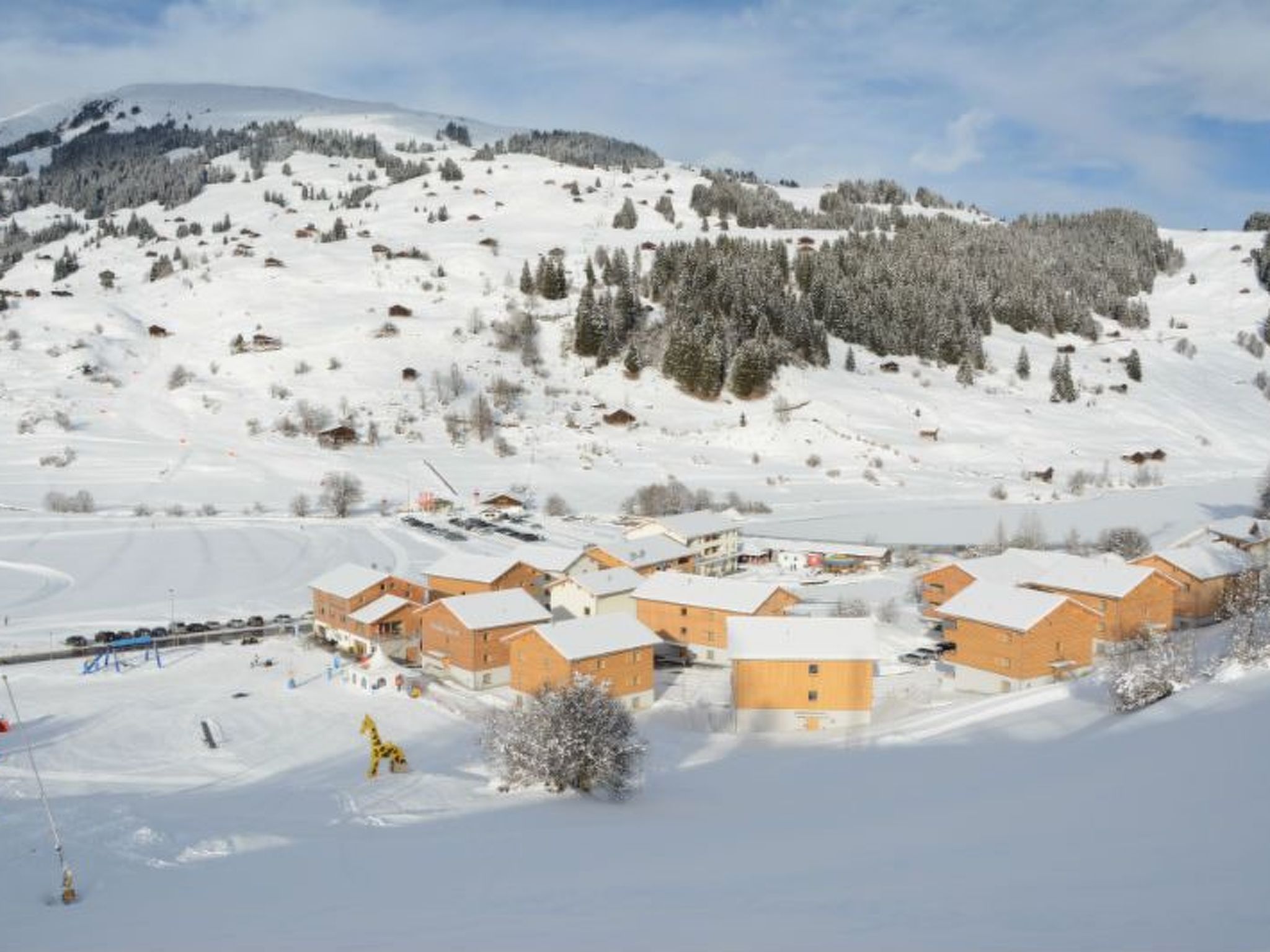 A snow-covered mountain with a ski resort in the foreground, featuring multiple buildings with snow-covered roofs.