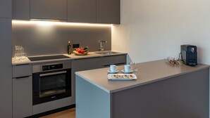 Une cuisine moderne équipée d’un four encastré, d’un évier et d’un plan de travail sur lequel se trouvent une machine à café et une assiette de viennoiseries.