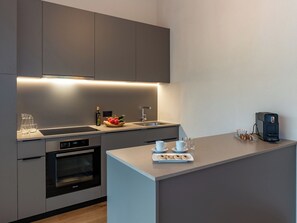 A modern kitchen with a built-in oven, a sink, and a countertop with a coffee maker and a plate of pastries. - Pradas Resort Brigels, (Breil/Brigels), 65055B by Interhome (Breil/Brigels)
