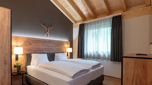 Une chambre d’hôtel moderne avec un plafond en bois, un grand lit avec du linge de lit blanc, deux lampes de chevet, une décoration murale représentant une tête de cerf et une fenêtre avec des rideaux.
