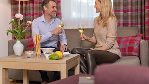 Un hombre y una mujer sentados en un sofá, sosteniendo copas de vino, con una mesa delante.