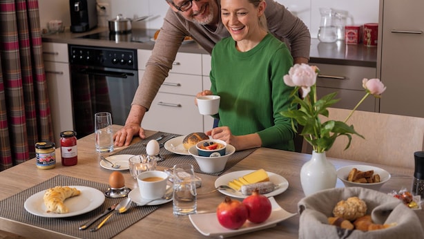 Una escena de desayuno con una mesa, platos, tazas y un florero con flores.