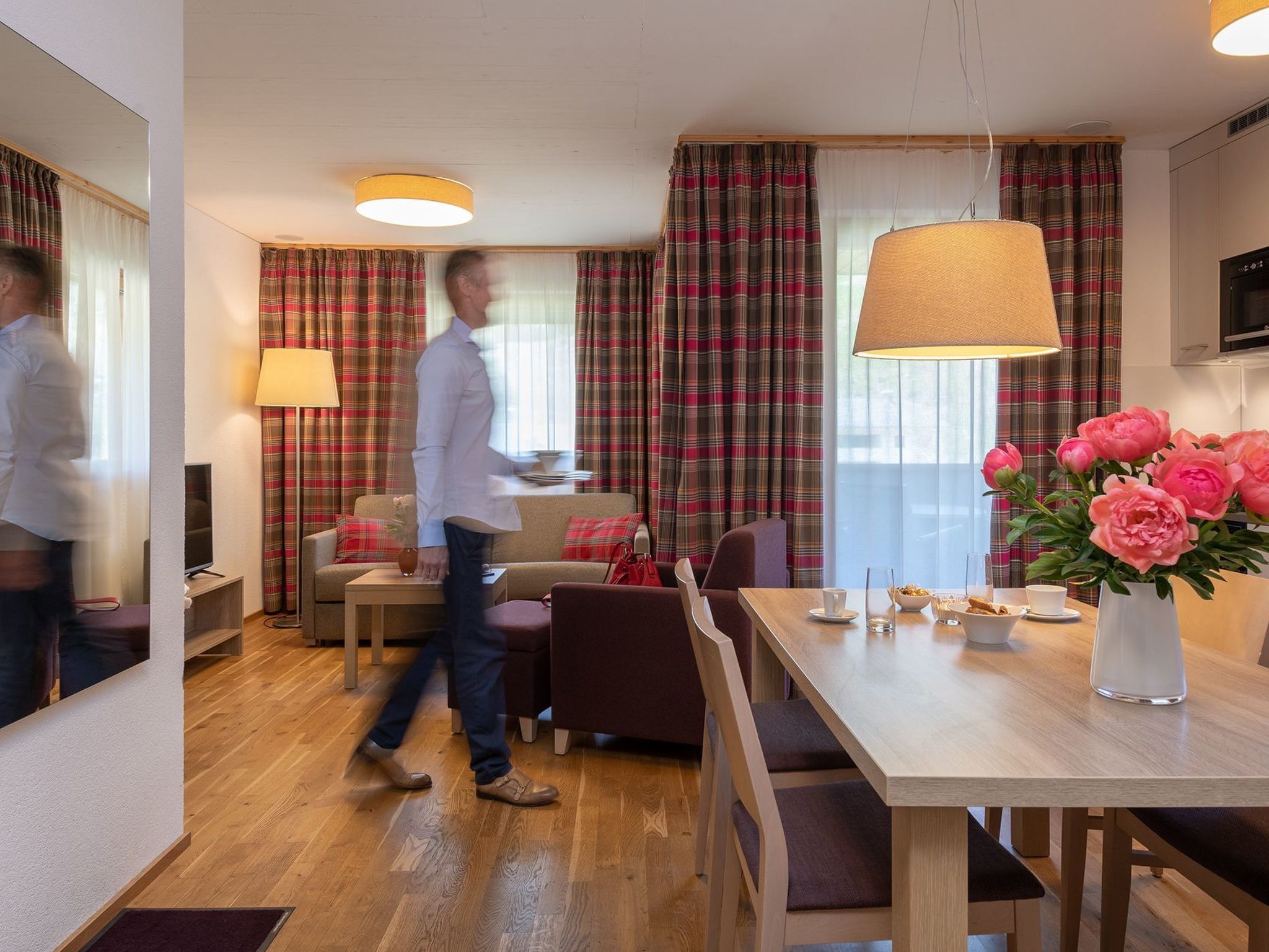 Ein modernes Hotelzimmer mit Essbereich, einer Couch, einem Fernseher und einem großen Fenster mit Vorhängen.