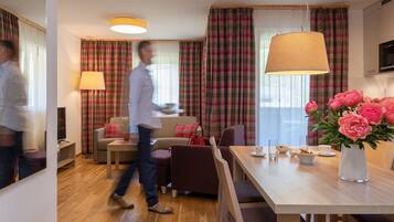 Ein modernes Hotelzimmer mit Essbereich, einer Couch, einem Fernseher und einem großen Fenster mit Vorhängen.