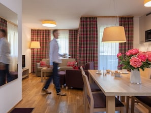 Une chambre d’hôtel moderne dotée d’un coin repas, d’un canapé, d’une télévision et d’une grande fenêtre avec des rideaux.