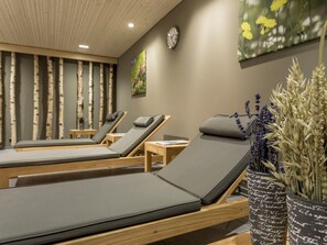 A spa room with three wooden loungers, a wall clock, and a painting of flowers. - Pradas Resort Brigels, (Breil/Brigels), 65055B by Interhome (Breil/Brigels)
