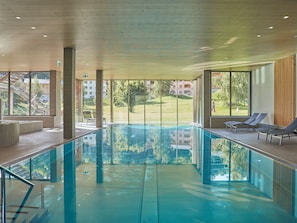 Une piscine avec des parois en verre transparent, des chaises longues et une vue sur un paysage verdoyant.