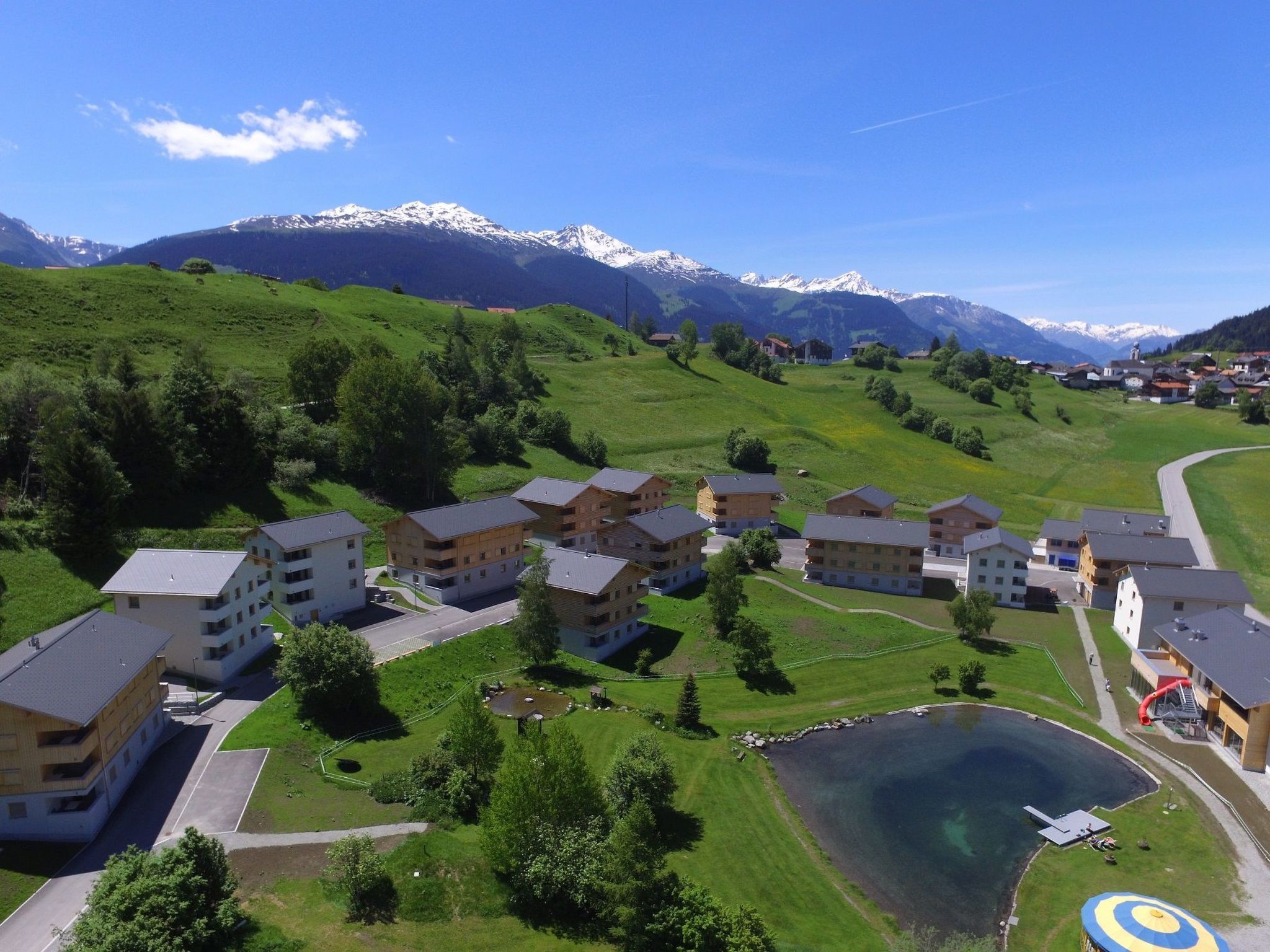 A residential area with multi-story buildings, a small lake, and mountains in the background.