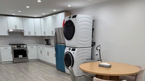 Una cocina moderna con armarios blancos, horno empotrado, lavadora y una mesa de comedor redonda de madera con sillas.