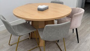 Una mesa redonda de madera con cuatro sillas, una con estructura dorada y las demás con tapicería gris.