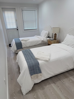 A bedroom with two single beds, a bedside table with a lamp, and a door with a window.