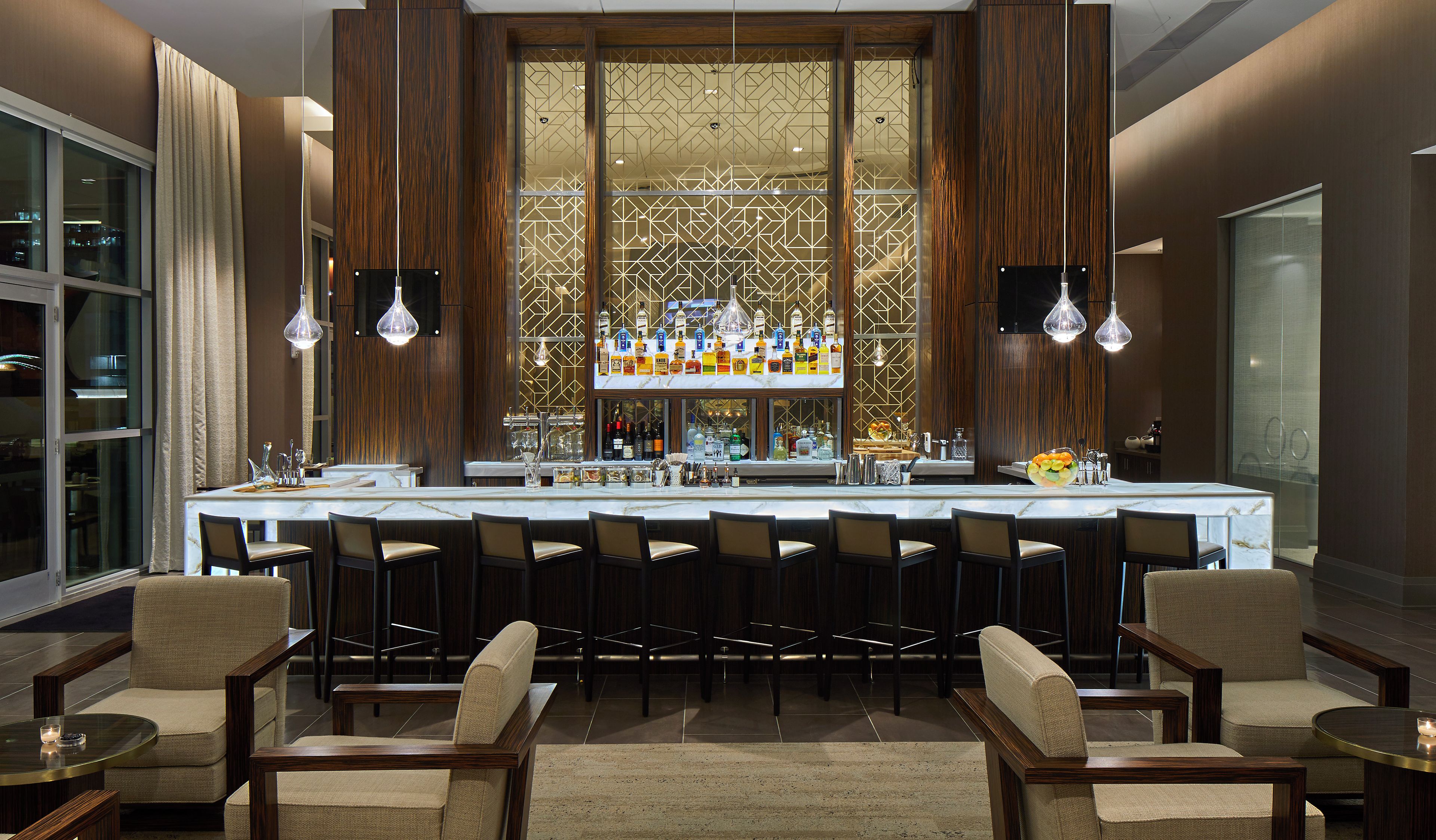 A bar area with a long counter, multiple chairs, and a decorative partition with bottles.