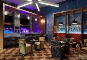 Zona bar con pavimento a scacchi, sgabelli da bar e bancone con bottiglie.
