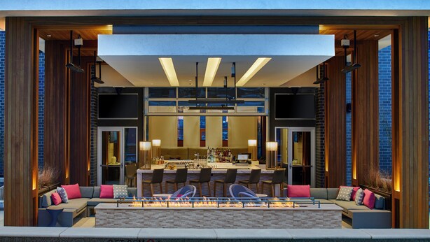 Un área de bar moderna al aire libre con piscina, asientos y una chimenea.