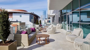Una terraza en la azotea con mobiliario de mimbre, una planta en maceta y vistas del horizonte urbano.