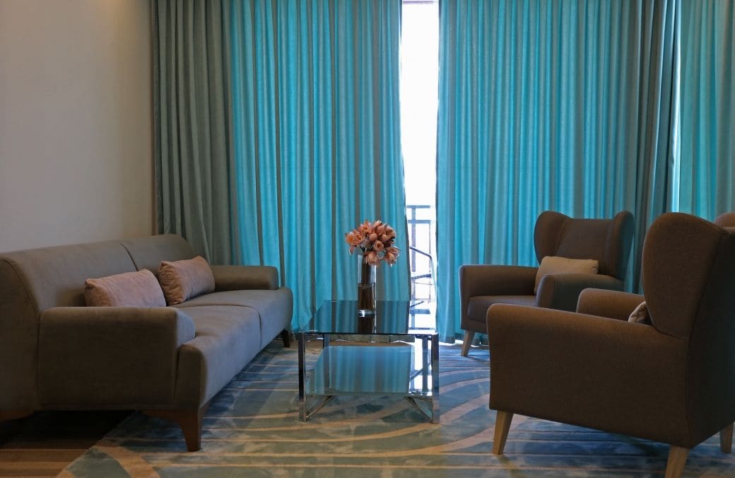 Una sala de estar con sofá, sillón y una mesa de centro de vidrio con un jarrón de flores.