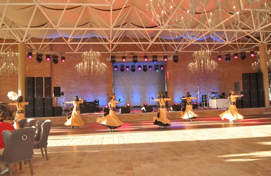 Una función de danza en un escenario con un fondo de pared de ladrillo, candelabros y un techo con diseño geométrico.