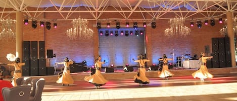 Una función de danza en un escenario con un fondo de pared de ladrillo, candelabros y un techo con diseño geométrico.