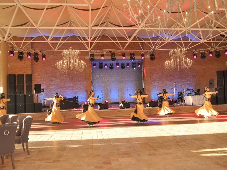 Une représentation de danse sur une scène dont le décor est constitué d’un mur en briques, de lustres et d’un plafond orné de motifs géométriques.
