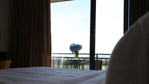 A hotel room with a large bed, a window with curtains, and a view of greenery outside.